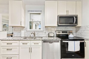 Una cocina con gabinetes blancos, un microondas de acero inoxidable, una estufa negra y un lavavajillas.