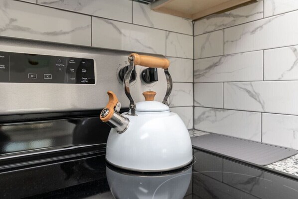 A white kettle with wooden handles on a modern kitchen stove.