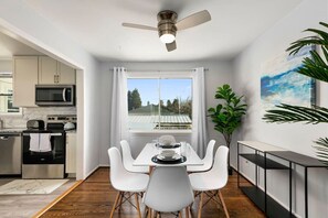 A modern kitchen with white cabinetry, a microwave, and a dining area with white chairs and a table.