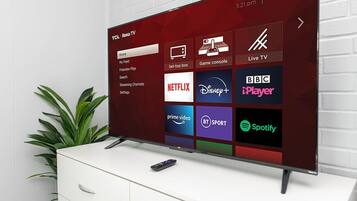A TCL Roku TV with a red interface displaying various streaming services.