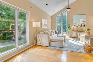 A spacious living room with a large window, a sofa set, a floor lamp, and a painting on the wall. - Arlington Oasis 7 Br (Jamestown)