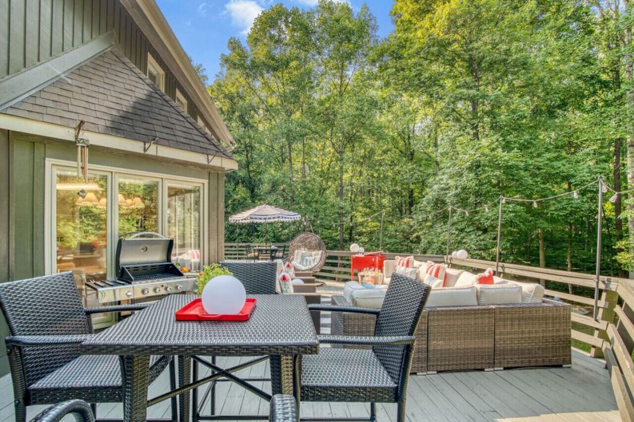 Een terras met buitenmeubilair, een barbecue en uitzicht op een bos.