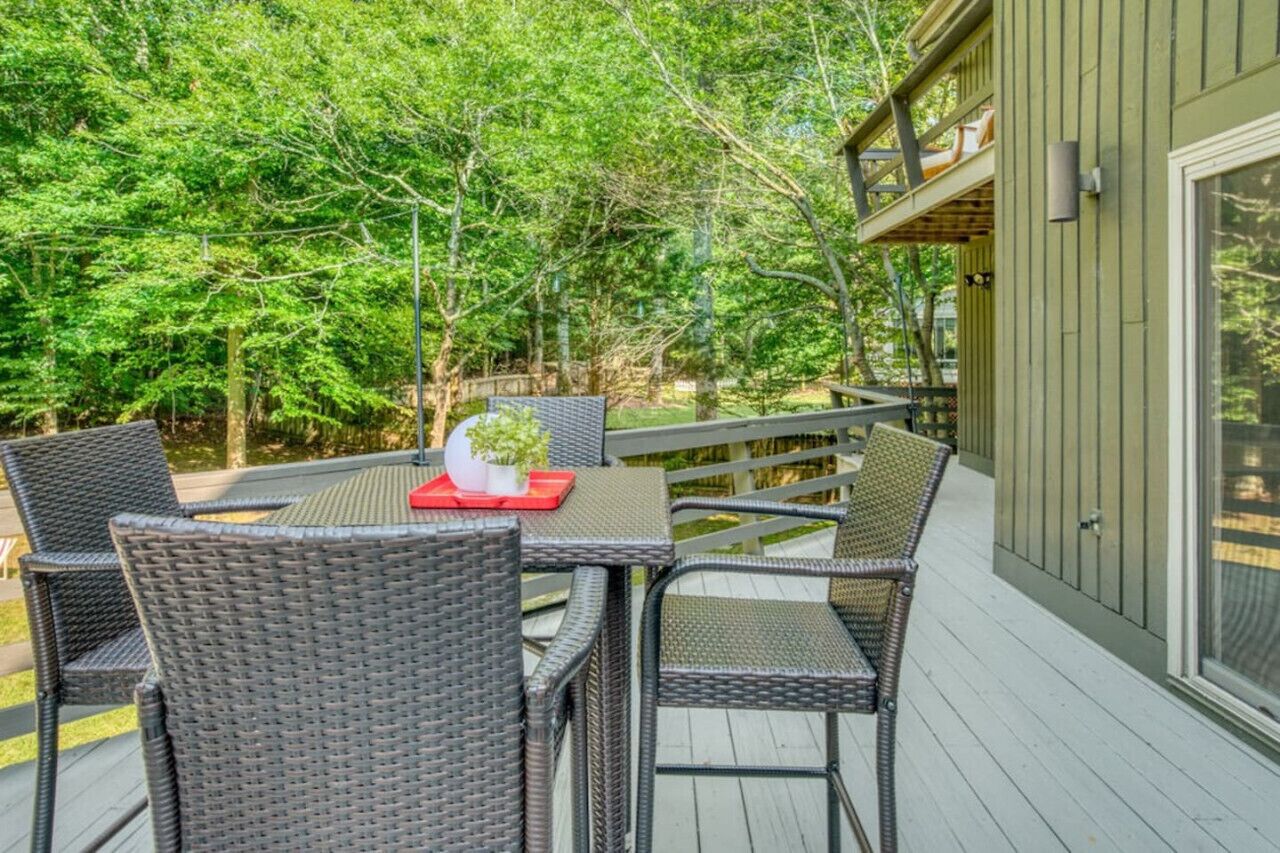 An outdoor deck with wicker furniture and a table, surrounded by lush greenery.