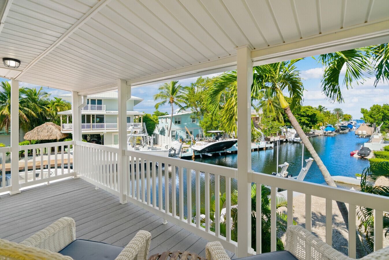 A covered outdoor area with a view of a marina, boats, and palm trees.
