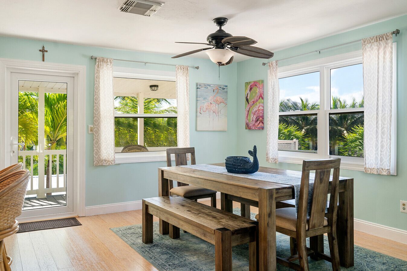 A dining area with a wooden table and chairs, a ceiling fan, and large windows with curtains.