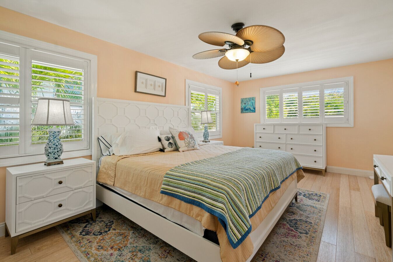 Une chambre à coucher comprenant un lit, des tables de chevet, une commode, un ventilateur de plafond et des fenêtres équipées de stores.