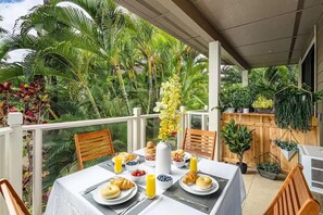 A balcony with a table set for breakfast, surrounded by lush tropical plants. - Spacious Ground Floor Maui Retreat, Grand Champion (Kihei)