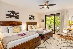 A hotel room with two beds, a ceiling fan, a dining area with a table and chairs, and a large window with a view of greenery. - Spacious Ground Floor Maui Retreat, Grand Champion (Kihei)
