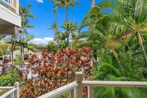 A balcony with a view of a tropical garden, palm trees, and a building in the background. - Spacious Ground Floor Maui Retreat, Grand Champion (Kihei)