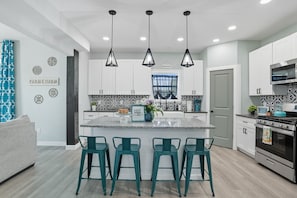 A modern kitchen with a central island, bar stools, pendant lights, and a stainless steel oven. - Renovated 6BR Near Grand Lake Fire Pit & Games (Grove)