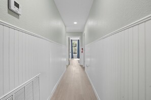 A hallway with white paneling, a ceiling light, and a door at the end. - Renovated 6BR Near Grand Lake Fire Pit & Games (Grove)