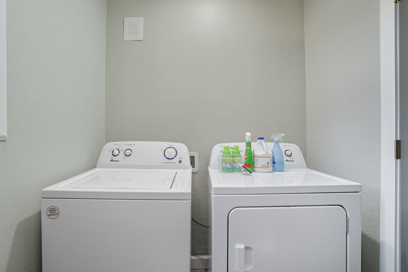 A laundry room with two white washing machines and a drying rack with cleaning supplies.