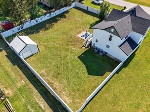 An aerial view of a property with a fenced yard, a detached garage, and a main building with a sloped roof. - Renovated 6BR Near Grand Lake Fire Pit & Games (Grove)