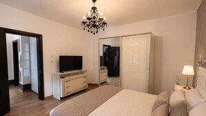 A bedroom with a bed, a television on a dresser, a chandelier, a wardrobe, and a nightstand with a lamp. - Elegant Boutique Apartment with Luxury Bedroom (Bucharest)