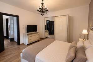 Ein Schlafzimmer mit Bett, Fernseher auf einer Kommode, einer Chandelüster, einem Kleiderschrank und einem Nachttisch mit Lampe.