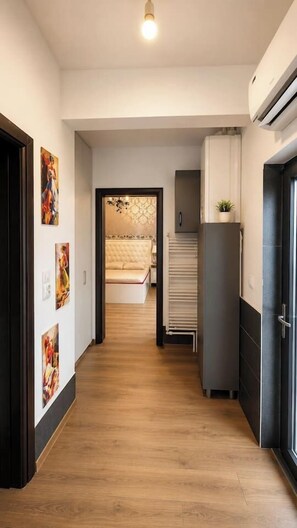 A hallway with a bed in the background, a refrigerator, and a door with a plant on top. - Elegant Boutique Apartment with Luxury Bedroom (Bucharest)