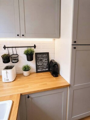 Eine Küche mit grauen Schränken, einer Holz Arbeitsplatte, einem Toaster, einer Kaffeemaschine und Topfpflanzen.