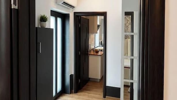 A hallway with a wooden floor leading to a kitchen area with white cabinets and an air conditioning unit. - Elegant Boutique Apartment with Luxury Bedroom (Bucharest)