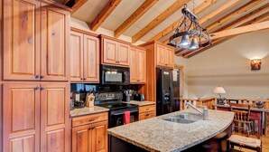 A kitchen with wooden cabinets, a granite countertop, a black stove, a microwave, and a refrigerator. - Appalachian Retreat (Blowing Rock)