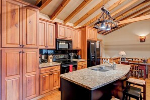 A kitchen with wooden cabinets, a granite countertop, a black stove, a microwave, and a refrigerator. - Appalachian Retreat (Blowing Rock)