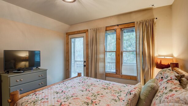 A bedroom with a bed, a TV on a dresser, and a window with curtains. - Appalachian Retreat (Blowing Rock)