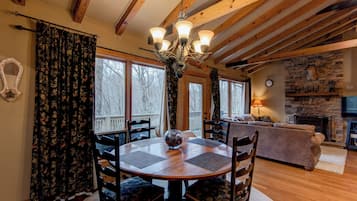 A cozy living room with a stone fireplace, wooden beams, and a large window overlooking a deck.