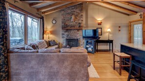 A cozy living room with a stone fireplace, a television, and a large window overlooking a vehicle. - Appalachian Retreat (Blowing Rock)