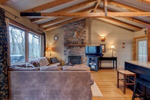 A cozy living room with a stone fireplace, a television, and a large window overlooking a vehicle. - Appalachian Retreat (Blowing Rock)