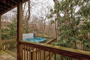 Una terraza de madera con un jacuzzi y vista a zona boscosa.