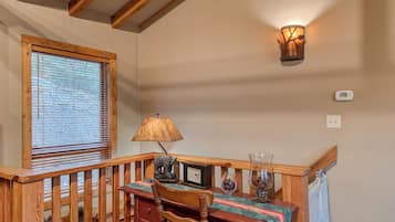 A wooden staircase with a railing, a table with chairs, a lamp, a wall-mounted light fixture, and a window with blinds.