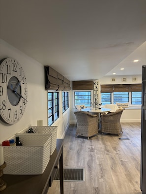 A modern kitchen with a large wall clock, wicker furniture, and a view through large windows. - Blue Heron 447 (Jensen Beach)