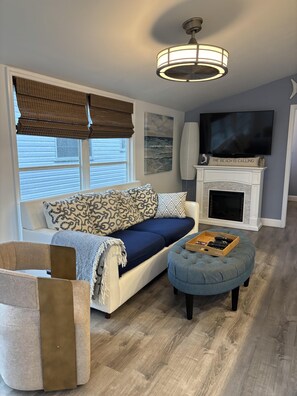 A living room with a sofa, ottoman, fireplace, TV, and a ceiling light fixture. - Blue Heron 447 (Jensen Beach)