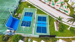 An aerial view of a sports complex with multiple basketball courts, a tennis court, and a surrounding fence. - Blue Heron 447 (Jensen Beach)