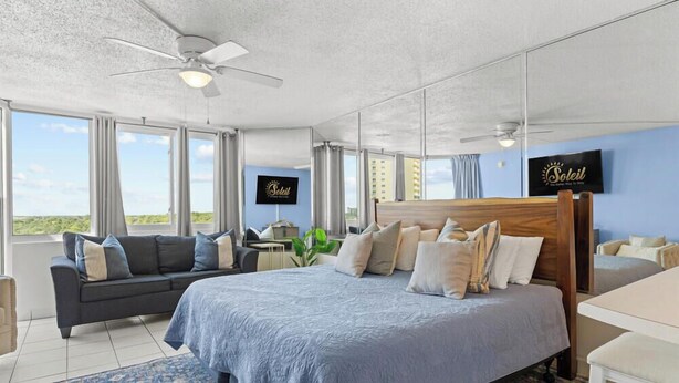 A hotel room with a bed, a sofa, a desk, and a view of the city. - Top of the Gulf 816 (Panama City Beach)