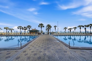 A swimming pool area with hexagonal tiles, palm trees, and a small pavilion. - Summit 625 (Panama City Beach)