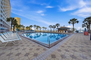 A swimming pool with lounge chairs, palm trees, and a building in the background. - Summit 625 (Panama City Beach)