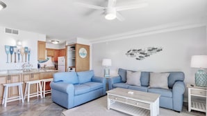 A modern living room with a blue sofa, white coffee table, and a kitchen area with wooden cabinets. - Summit 625 (Panama City Beach)
