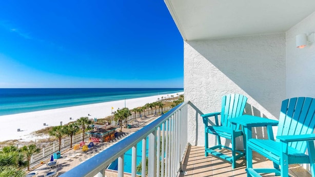 A balcony with a view of a beach and ocean, featuring a pool and blue chairs. - Summit 625 (Panama City Beach)