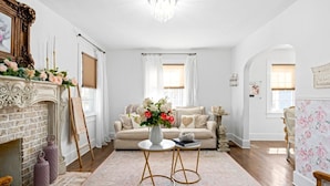 A living room with a fireplace, a sofa set, a coffee table, and a floral wall. - Pink House (Clarksville)