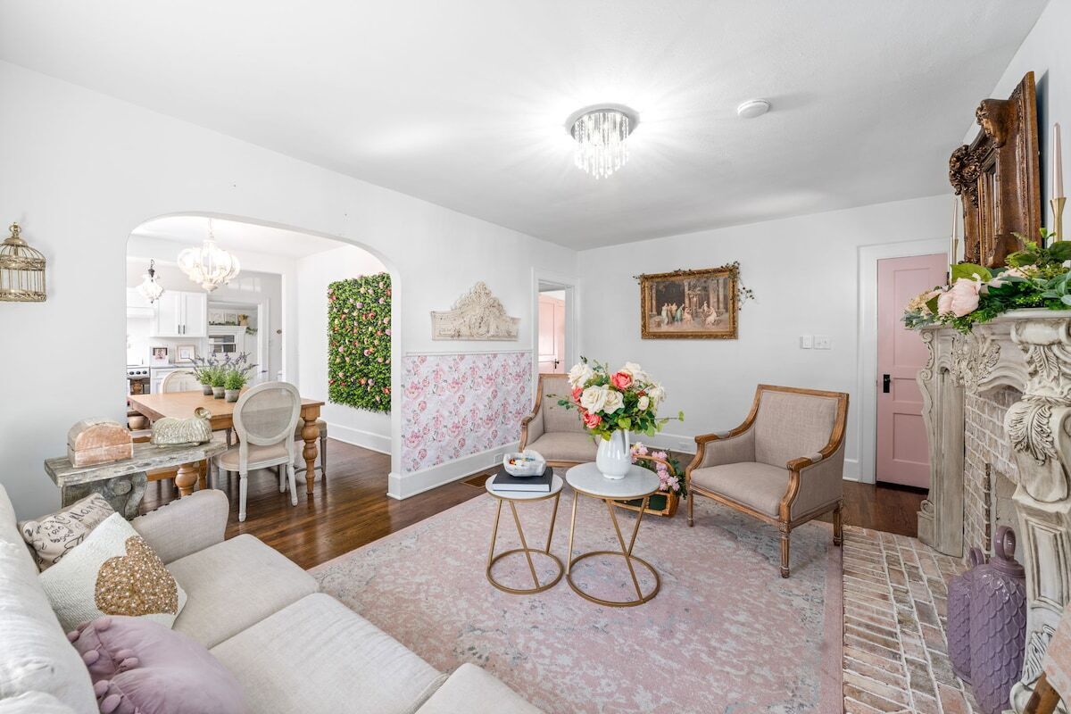 A spacious living room with a sofa, chairs, a coffee table, and a fireplace. There is a dining area with a table and chairs visible through an archway.
