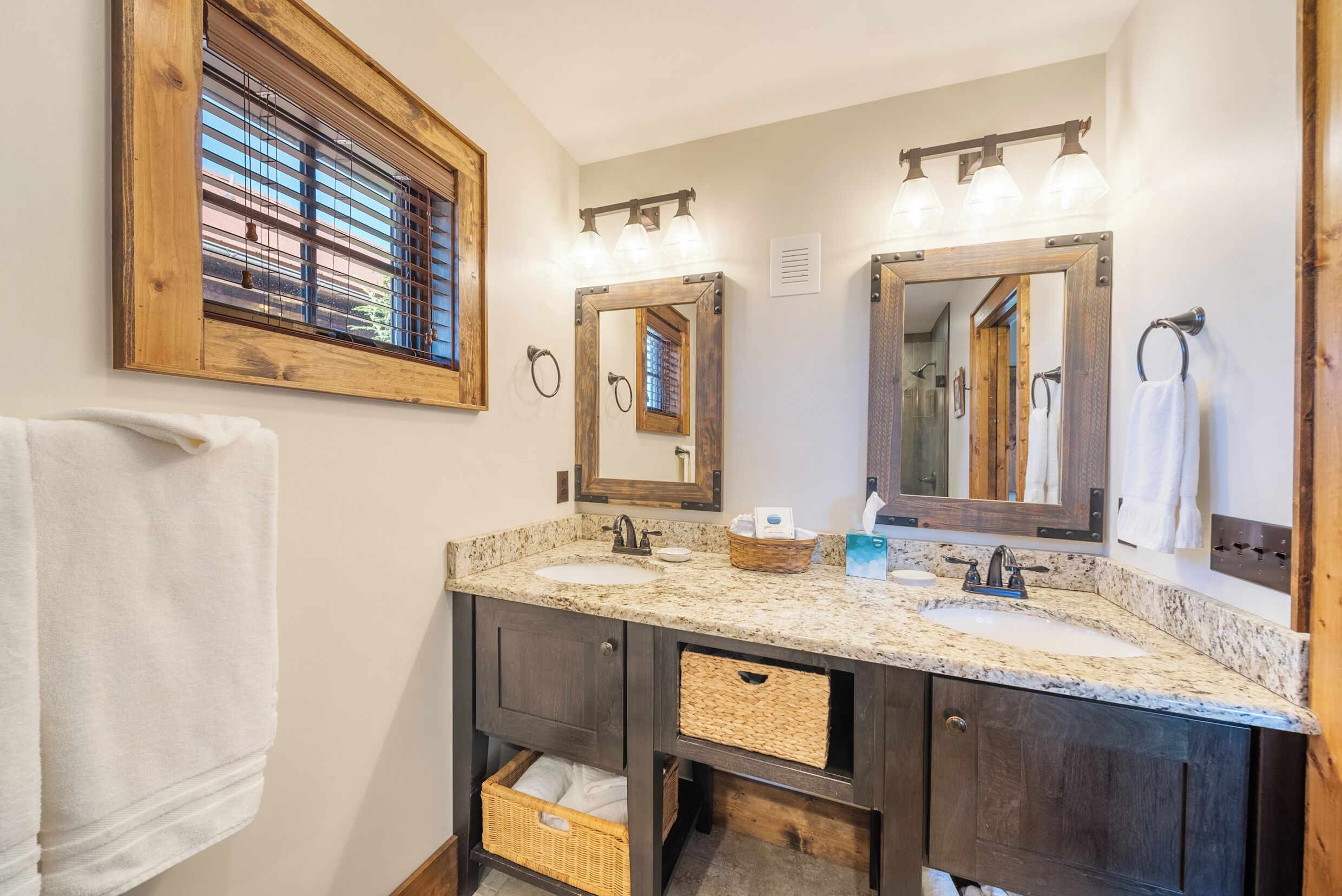 A bathroom with two sinks, a large mirror, and a window with blinds.
