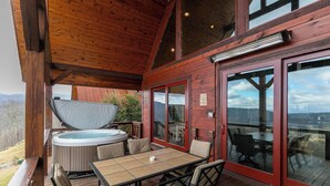 Eine Holzterrasse mit Whirlpool, Tisch und Stühlen mit Blick auf eine reizvolle Landschaft.