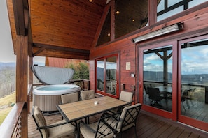 Eine Holzterrasse mit Whirlpool, Tisch und Stühlen mit Blick auf eine reizvolle Landschaft.