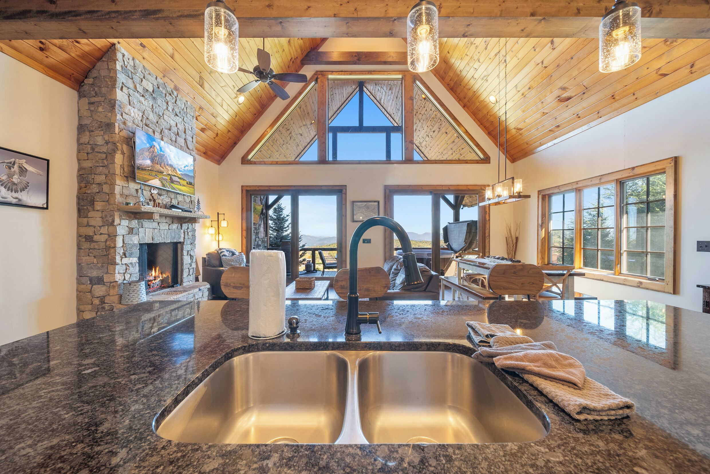 A kitchen with a stone fireplace, a large window, and a high ceiling with wooden beams.
