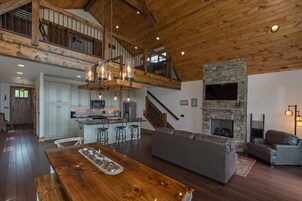 Amplia zona de estar estilo loft con cocina, techo de madera, chimenea de piedra y un nivel entrepiso.