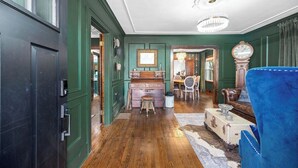 A room with a wooden floor, a blue armchair, a vintage desk, and a chandelier. - OC House 914 Crossland Ave (Clarksville)