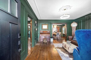 A room with a wooden floor, a blue armchair, a vintage desk, and a chandelier. - OC House 914 Crossland Ave (Clarksville)