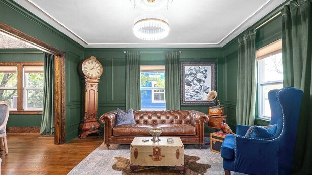 A room with a brown leather sofa, a blue armchair, a vintage clock, and a large painting on the wall. - OC House 914 Crossland Ave (Clarksville)