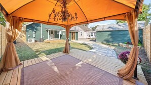 An outdoor patio area with a large umbrella providing shade, a wooden deck, and a view of a residential neighborhood. - OC House 914 Crossland Ave (Clarksville)