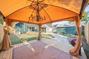An outdoor patio area with a large umbrella providing shade, a wooden deck, and a view of a residential neighborhood. - OC House 914 Crossland Ave (Clarksville)